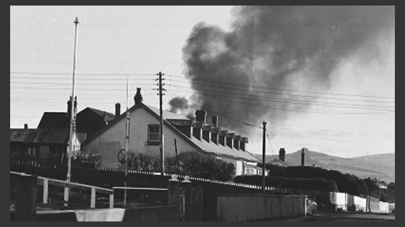 Un casa en Puerto Argentino con el humo de los estallidos de las bombas en el fondo. 