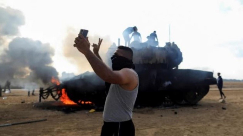 Un palestino se saca una selfie frente a un tanque israelí en llamas cerca de la frontera con la Franja de Gaza. (Foto: Reuters/Yasser Qudih).